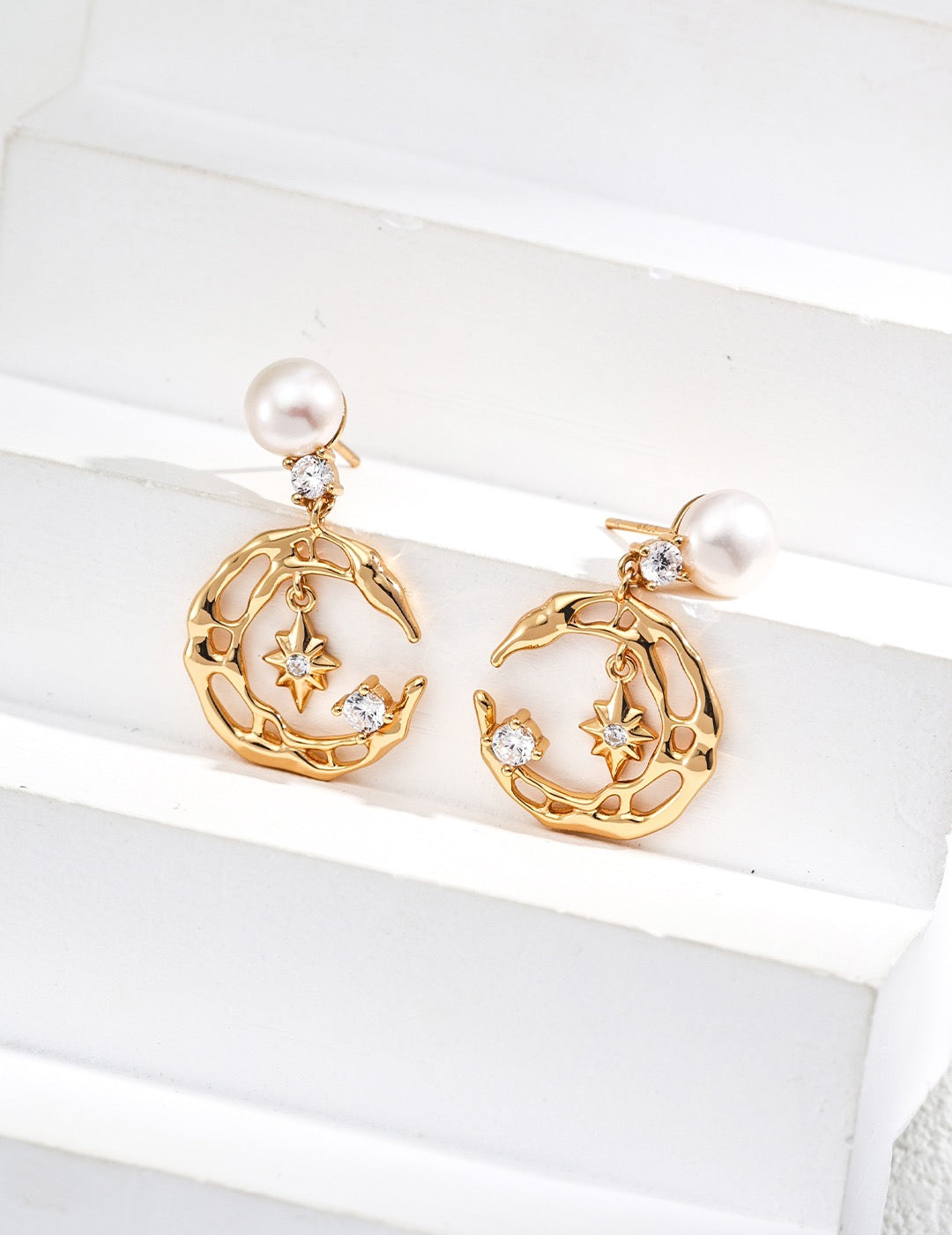 Gold moon and star earrings with pearls on a white surface