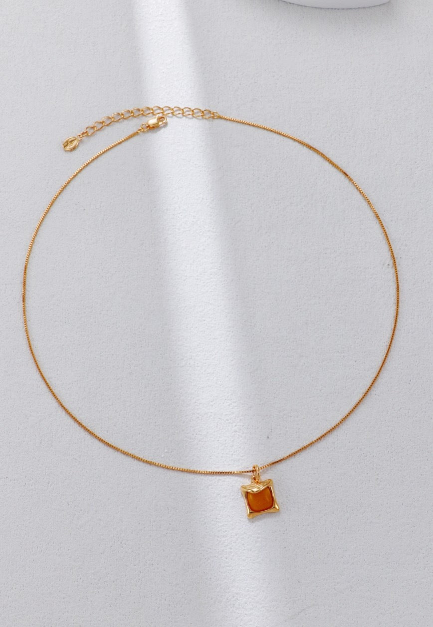 Gold necklace with a square pendant on a white background