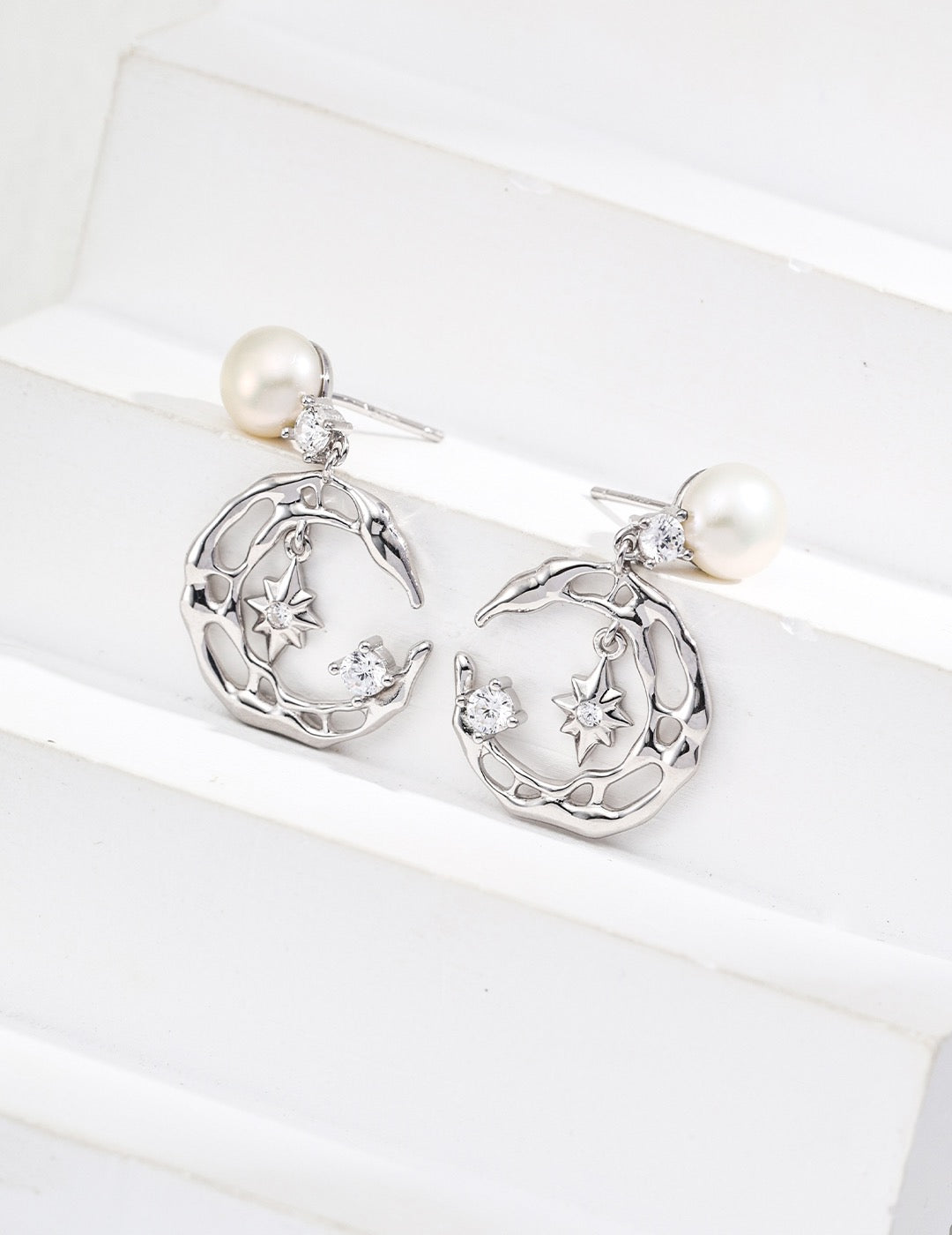 Silver earrings with moon and star designs on a white background