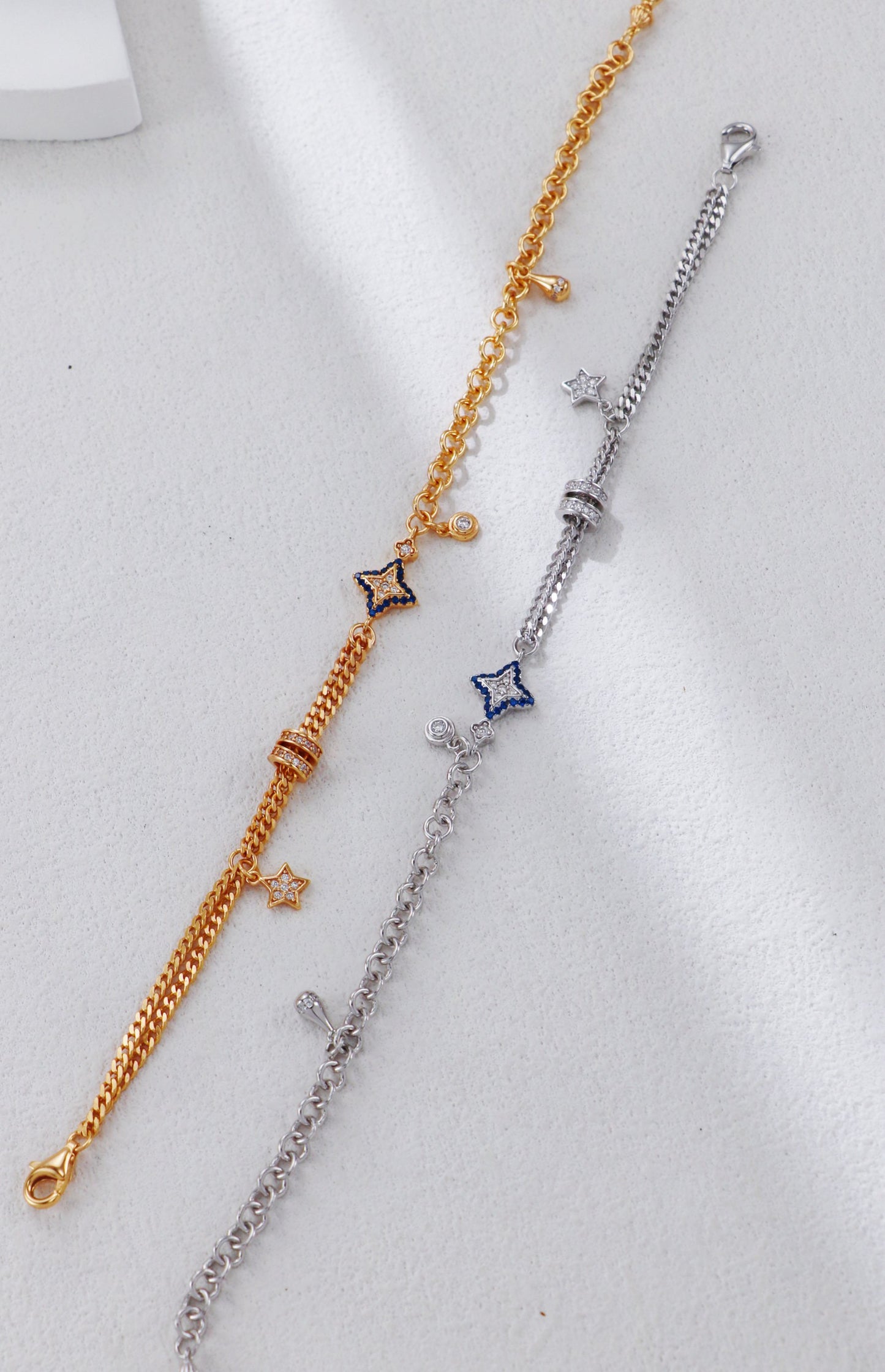 Two bracelets, one gold and one silver, with star-shaped charms on a light gray background.