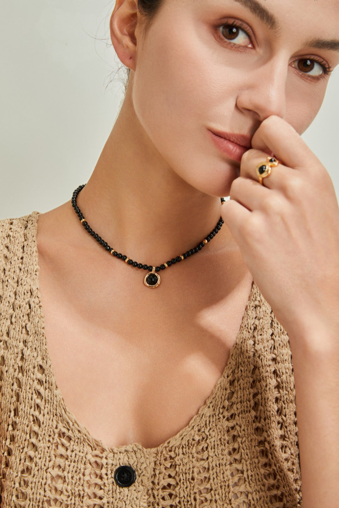 Woman wearing a black beaded necklace and ring against a neutral background