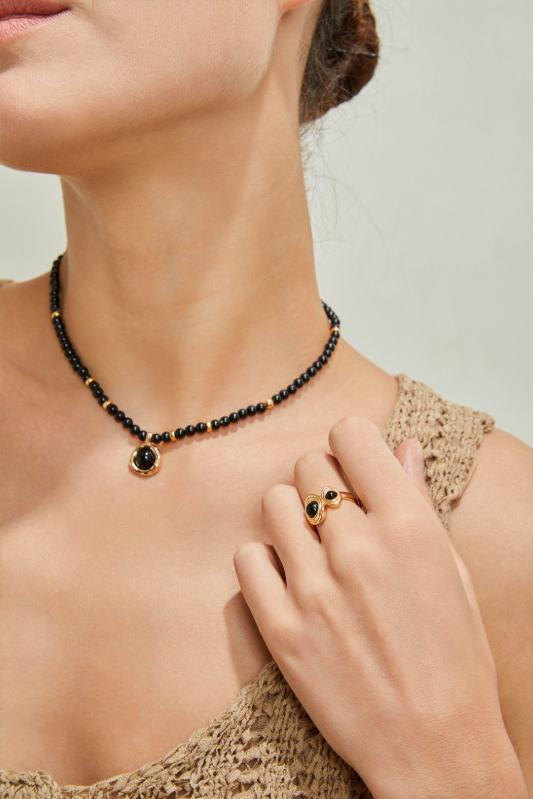 Woman wearing a black beaded necklace and ring with gold accents.