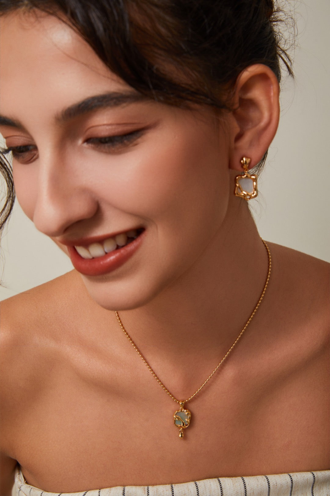Woman wearing gold earrings and necklace on a neutral background
