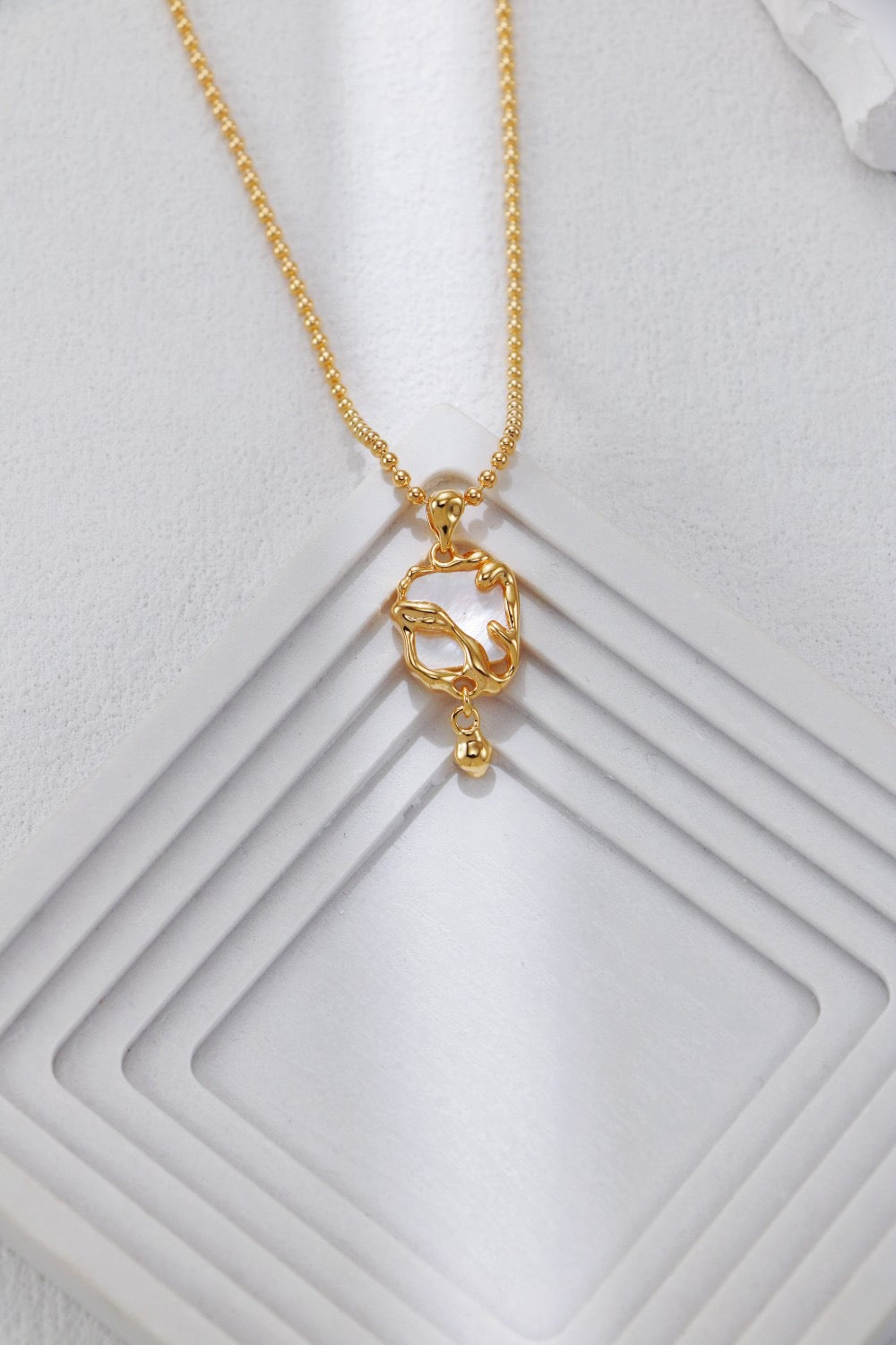 Gold necklace with a small pendant on a textured white surface