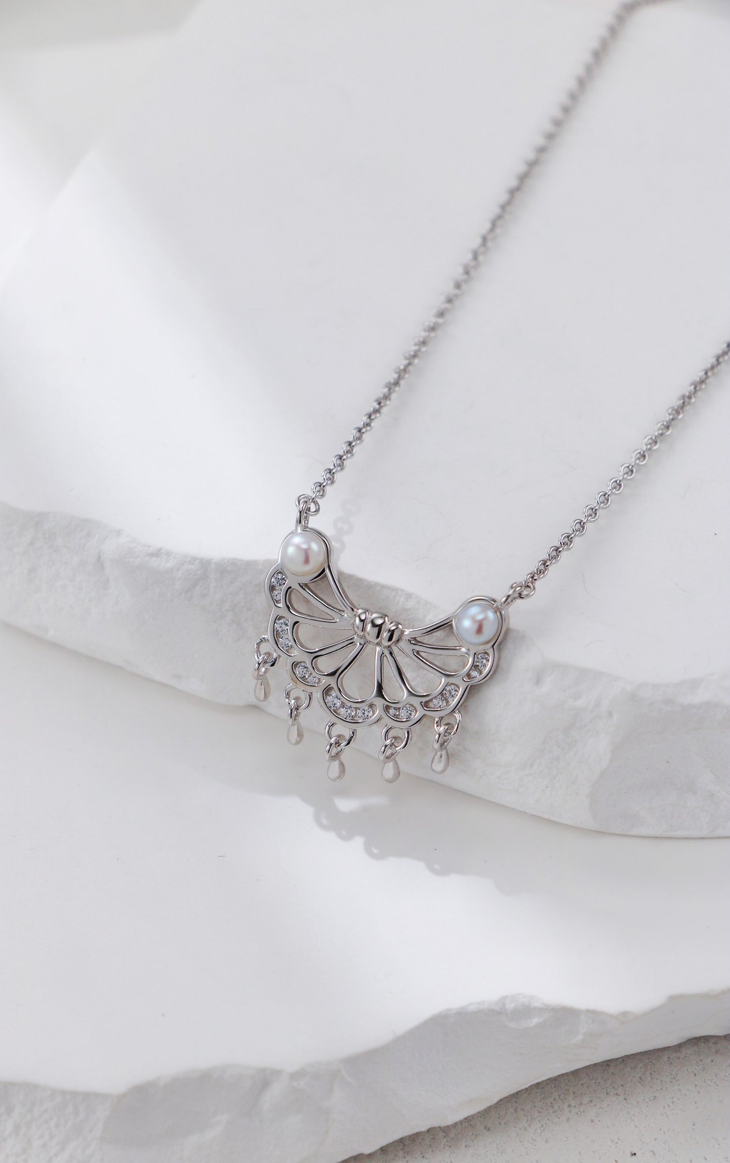 Silver necklace with butterfly design and pearls on a white background