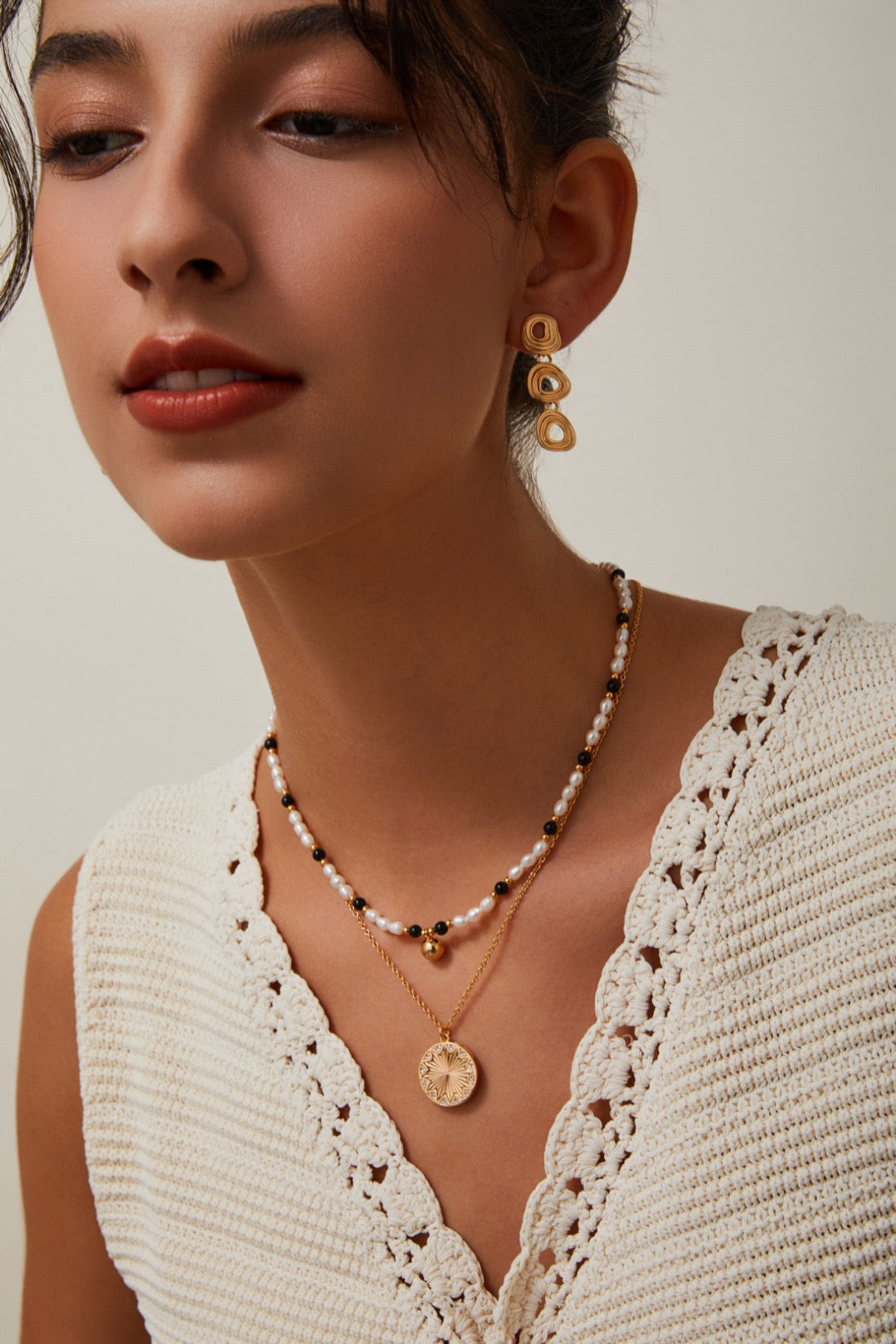 Close-up of a woman wearing gold earrings and necklaces against a neutral background