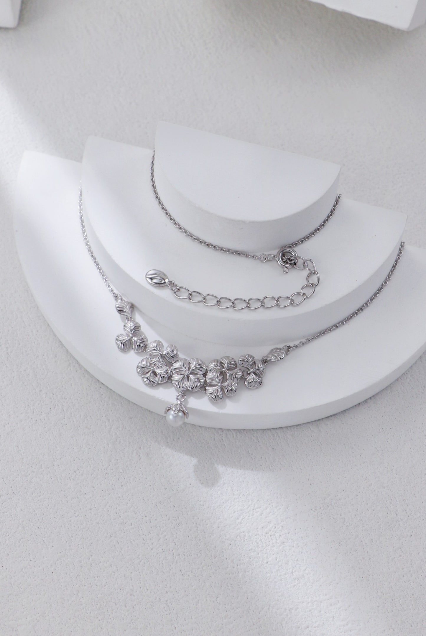 Silver necklace with floral design on a white stand