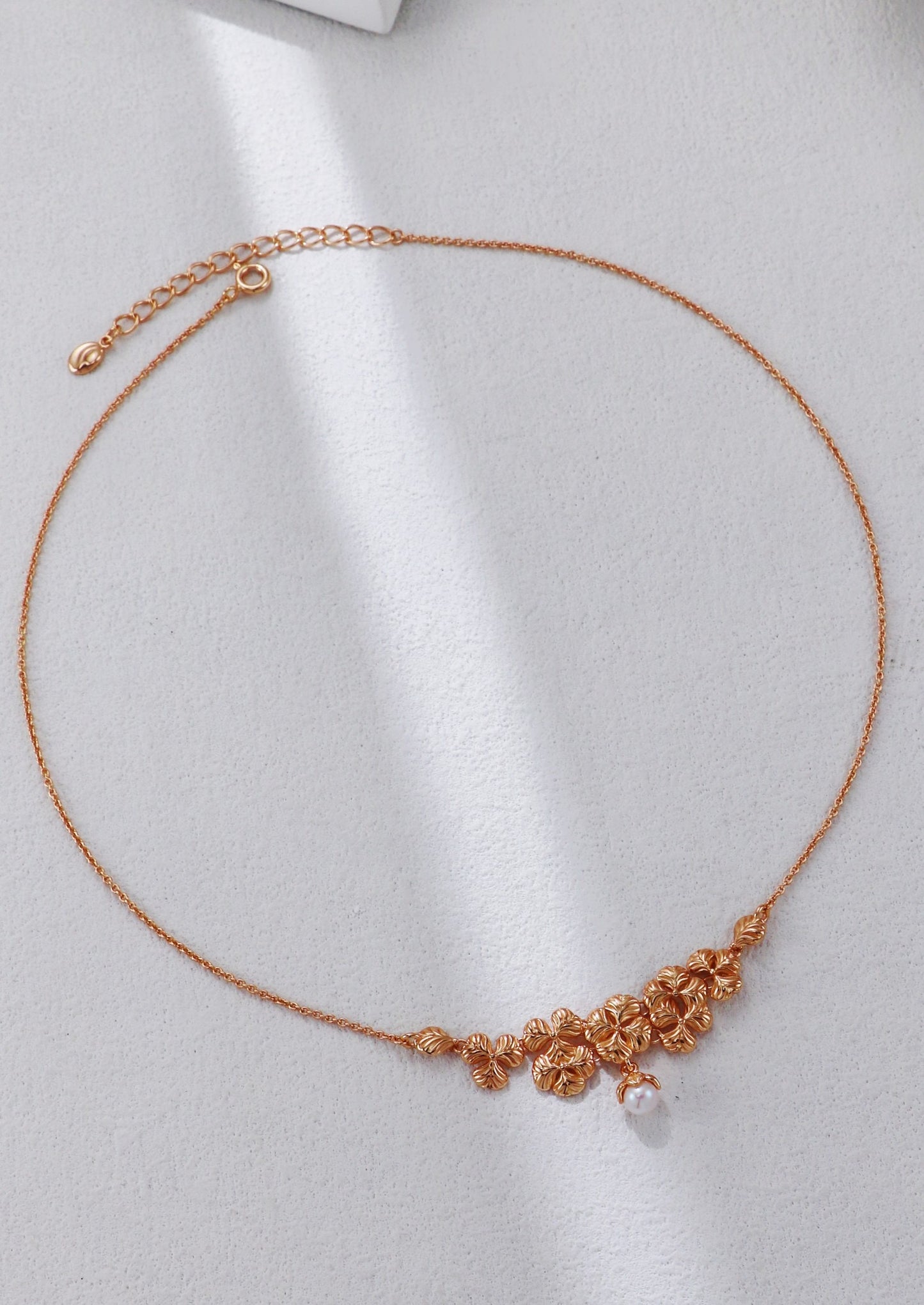 Rose gold necklace with floral design on a light gray background