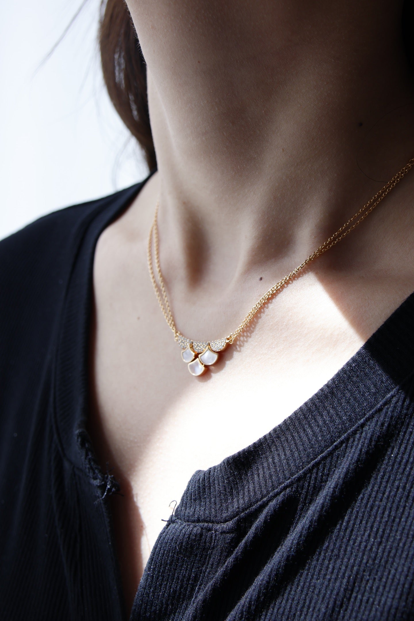 Close-up of a person wearing a delicate gold necklace with small stones.