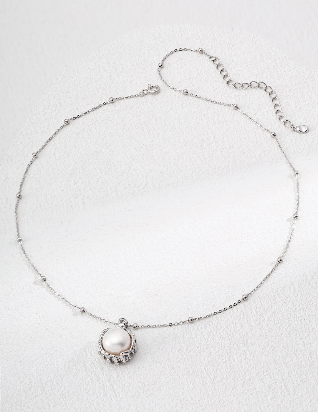 Silver anklet with a pearl charm on a light gray background