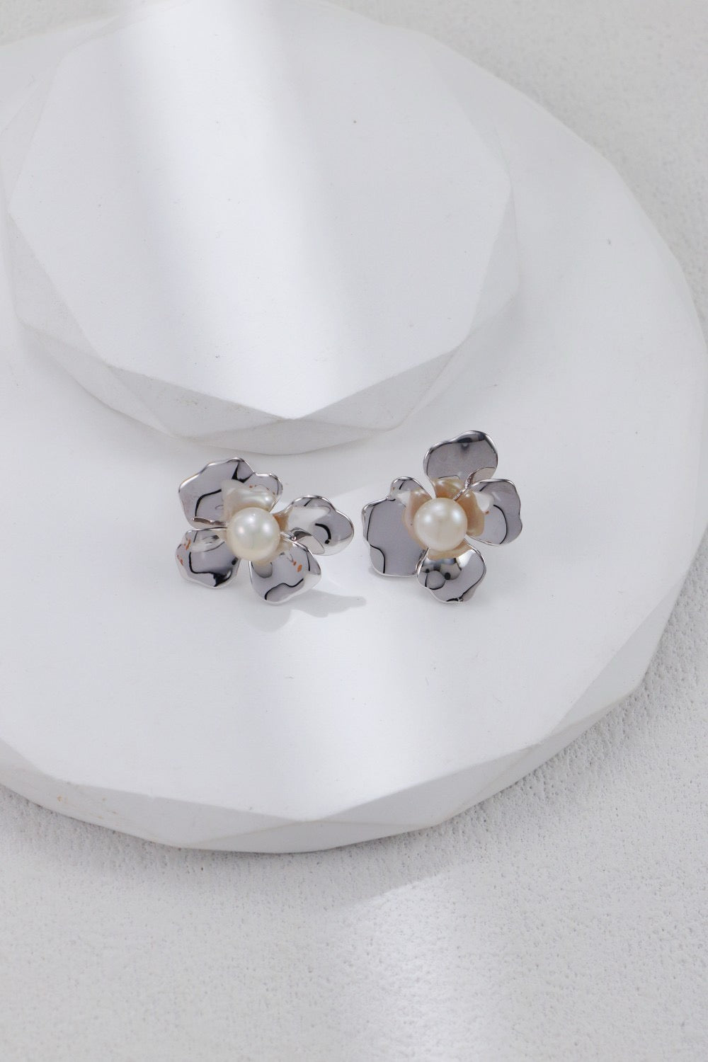 Pair of flower-shaped earrings with pearls on a white surface