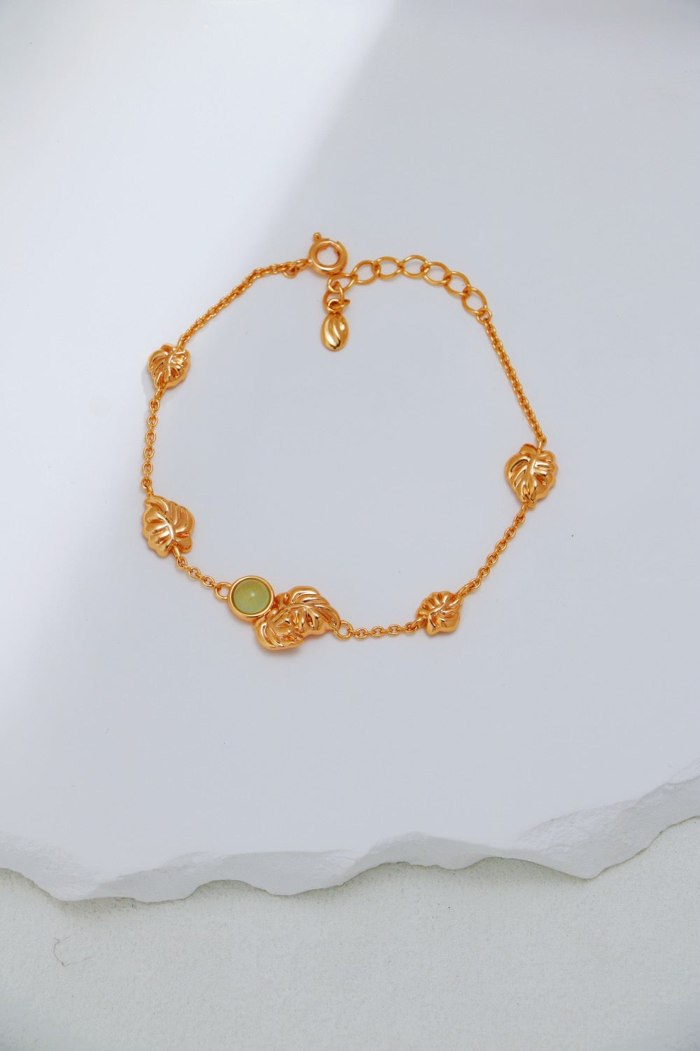 Gold bracelet with a green gemstone on a white fabric background