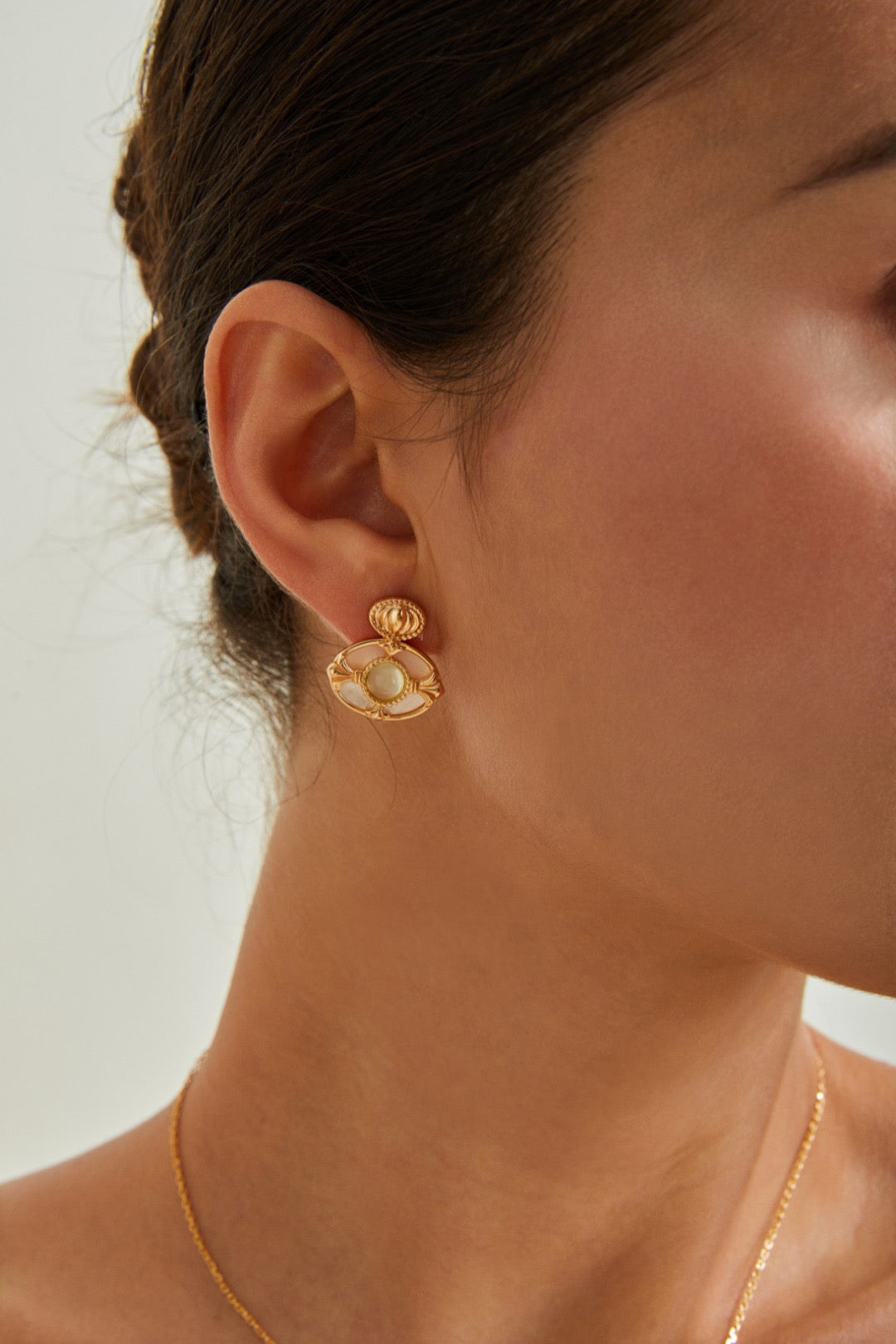 Close-up of a person wearing gold earrings with a neutral background