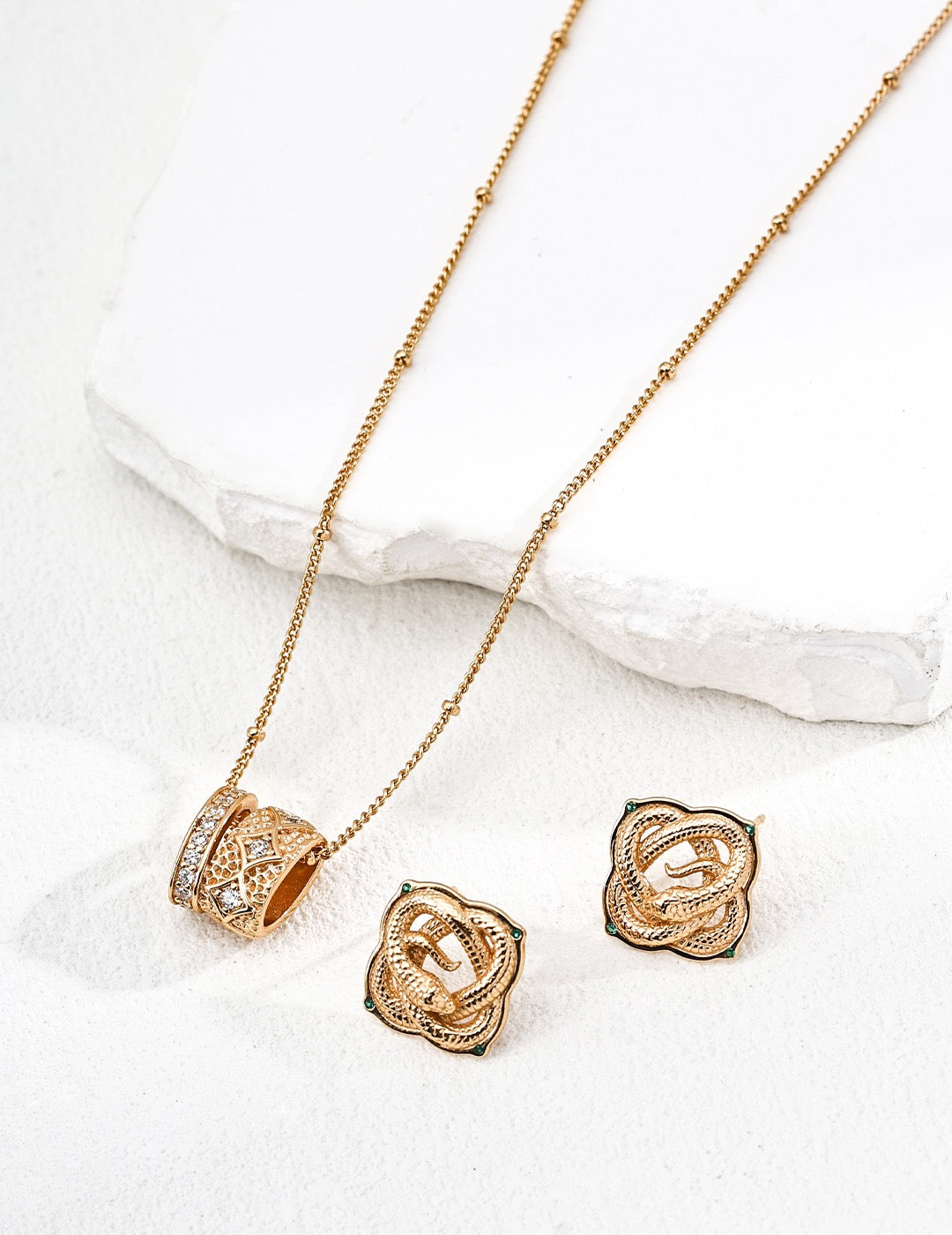 Gold necklace and earrings on a white surface
