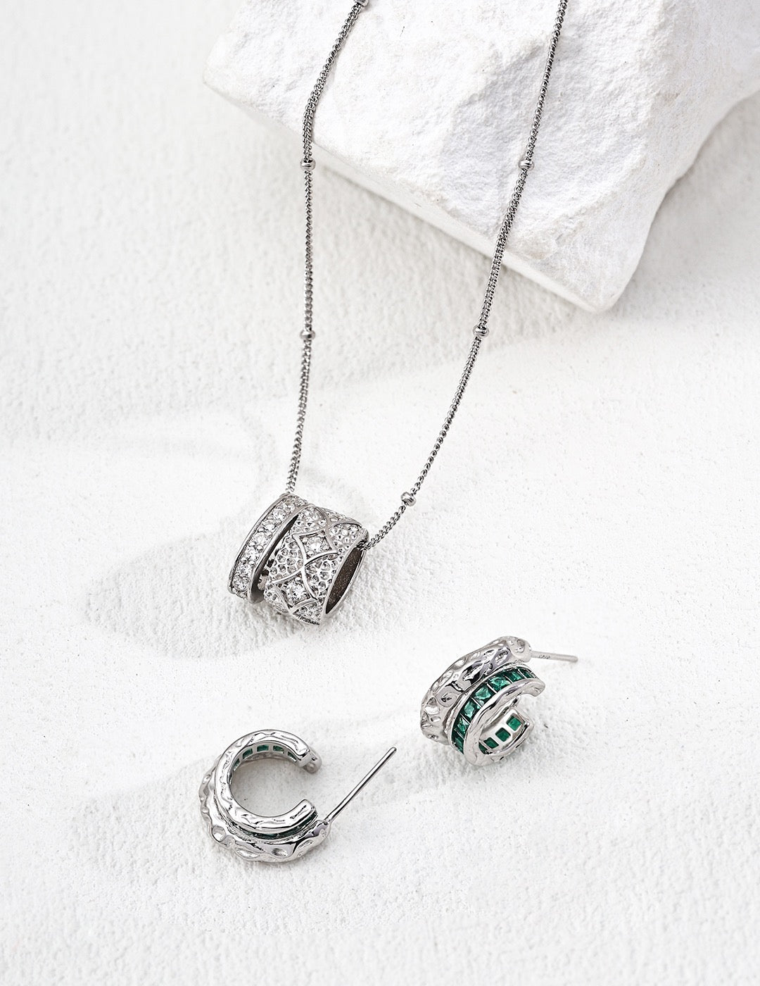 Silver jewelry set with pendant, earrings, and ring on a white surface