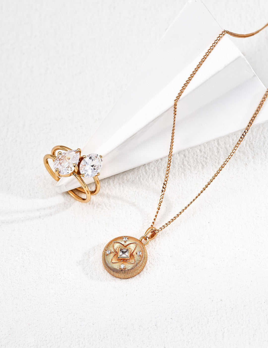 Rose gold necklace with circular pendant and matching ring on a white background
