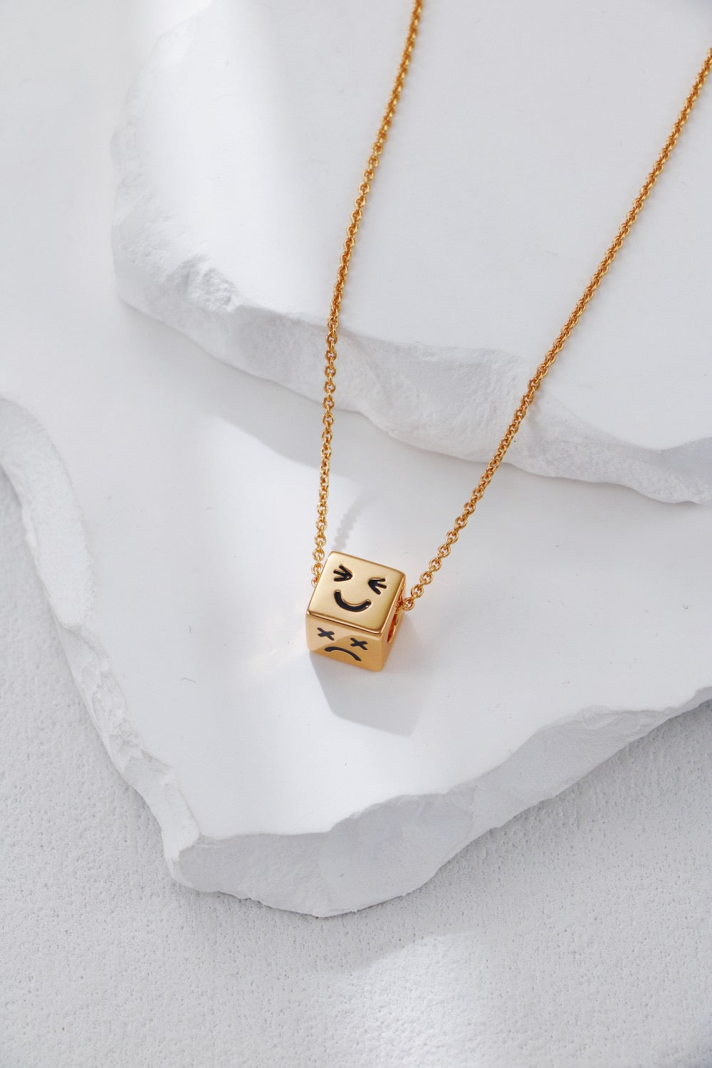 Gold necklace with a cube pendant featuring smiley faces on a white fabric background