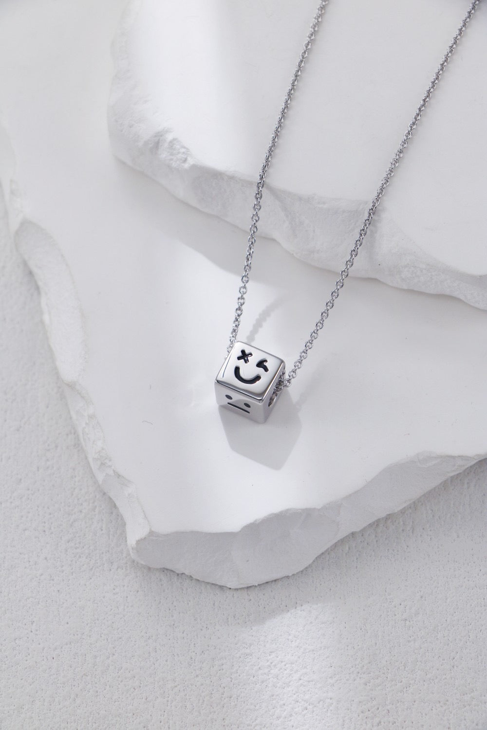 Silver necklace with a cube pendant featuring a smiley face on a white stone background