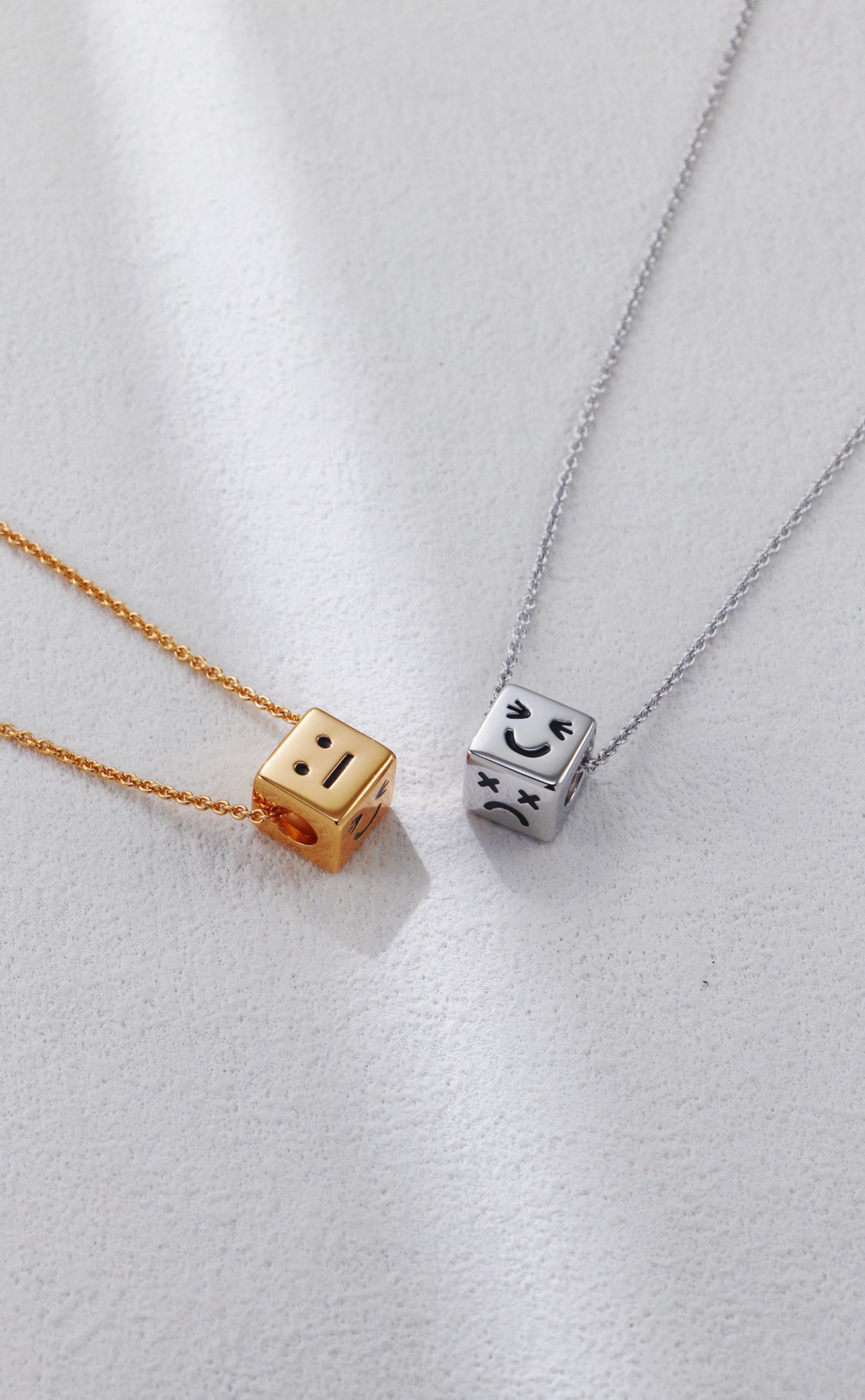Two dice-shaped pendants on gold and silver chains against a light background