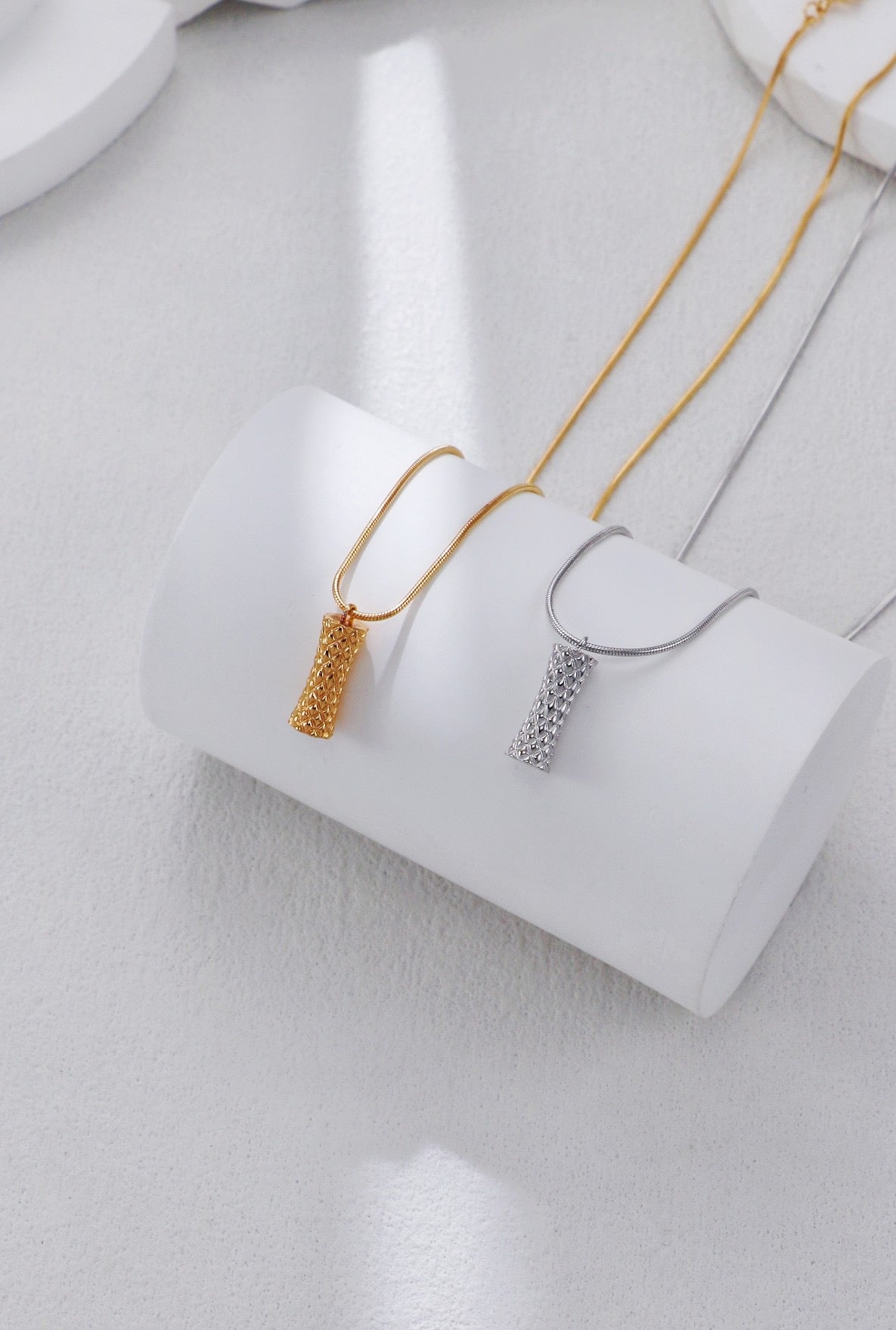 Two gold necklaces on a white stand against a light gray background