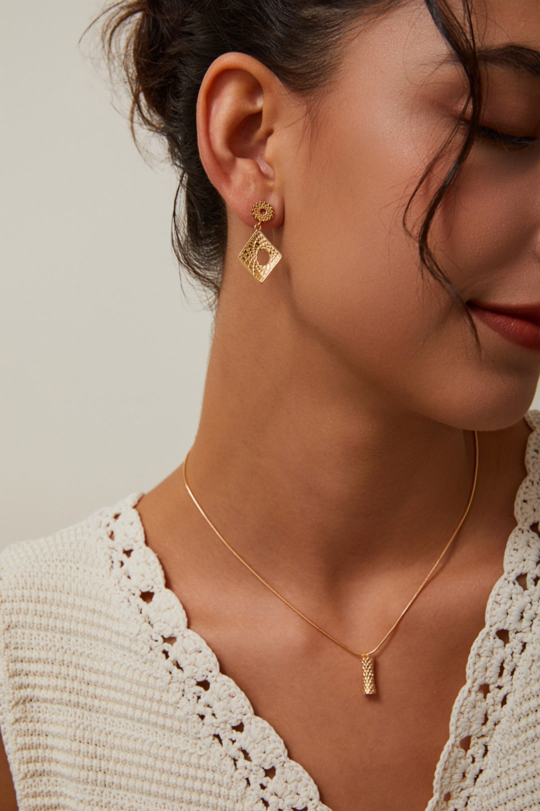 Close-up of a woman wearing gold earrings and necklace against a neutral background