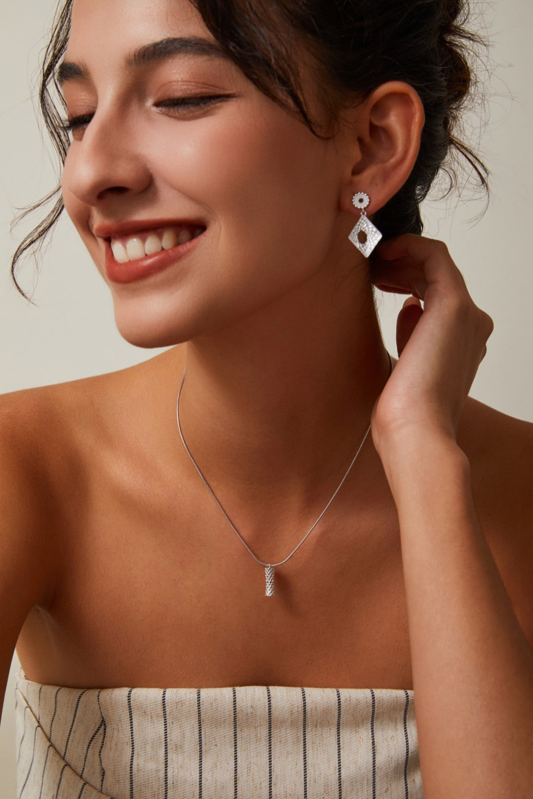 Woman wearing silver earrings and a necklace against a neutral background