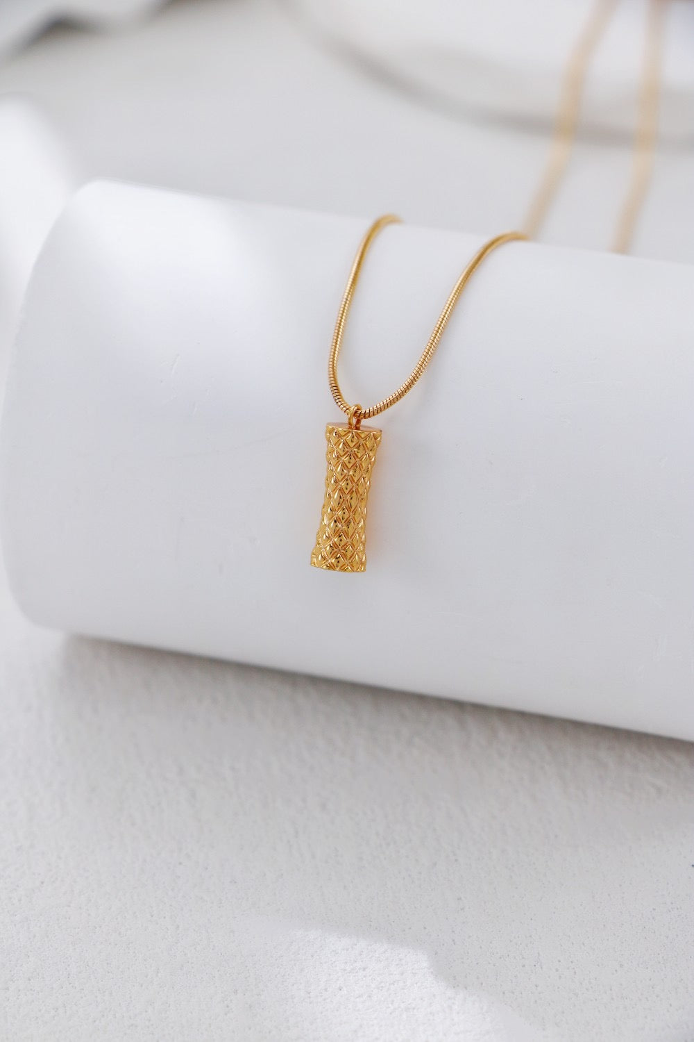 Gold necklace with a textured pendant on a white background