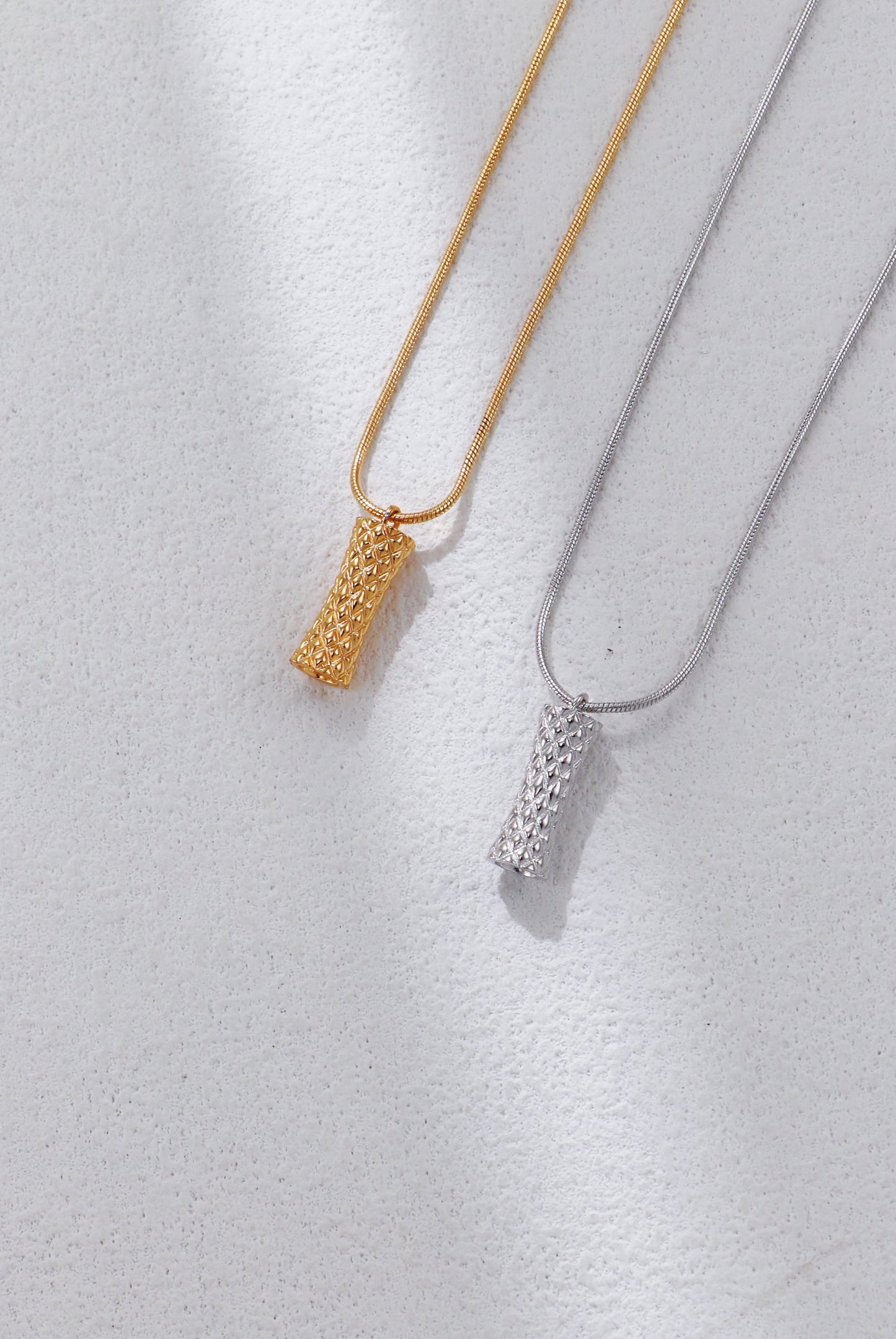 Two necklaces, one gold and one silver, on a light gray background.