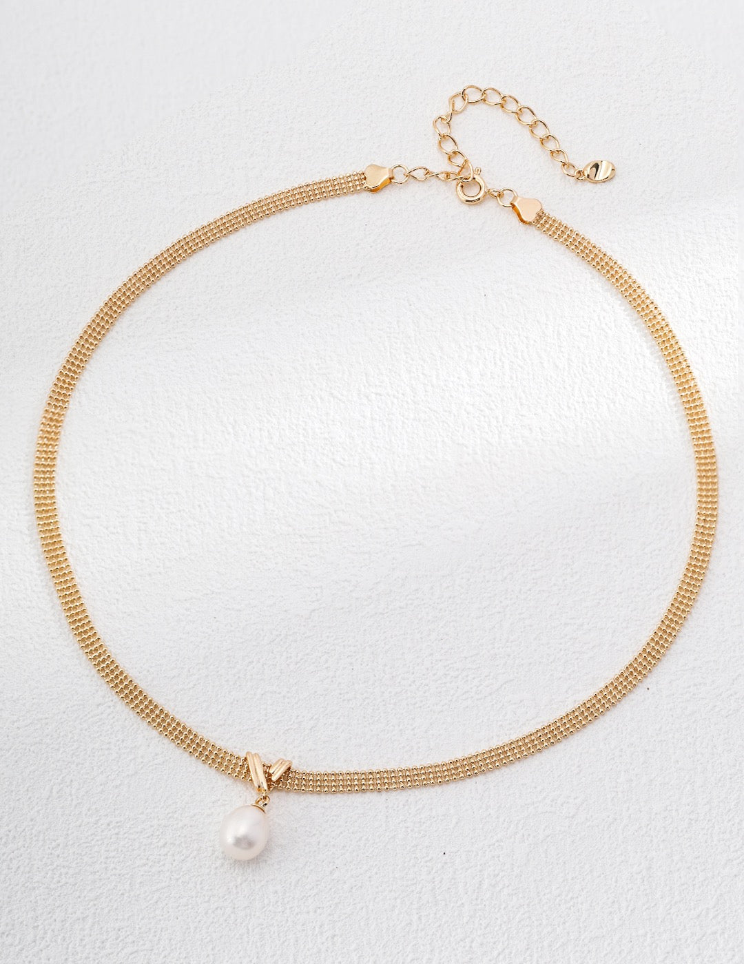 Gold necklace with a pearl pendant on a light gray background