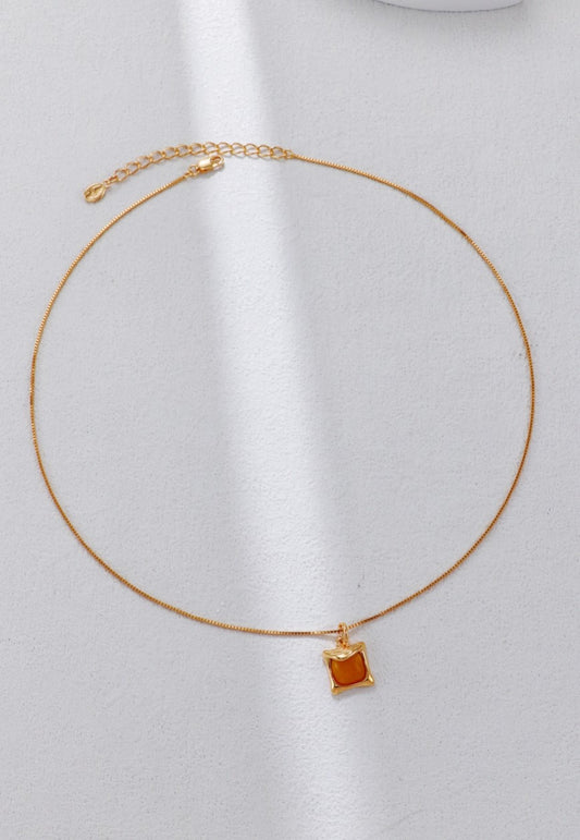 Gold necklace with a square pendant on a white background