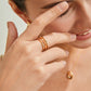 Close-up of a woman wearing gold jewelry including an earring, ring, and necklace.