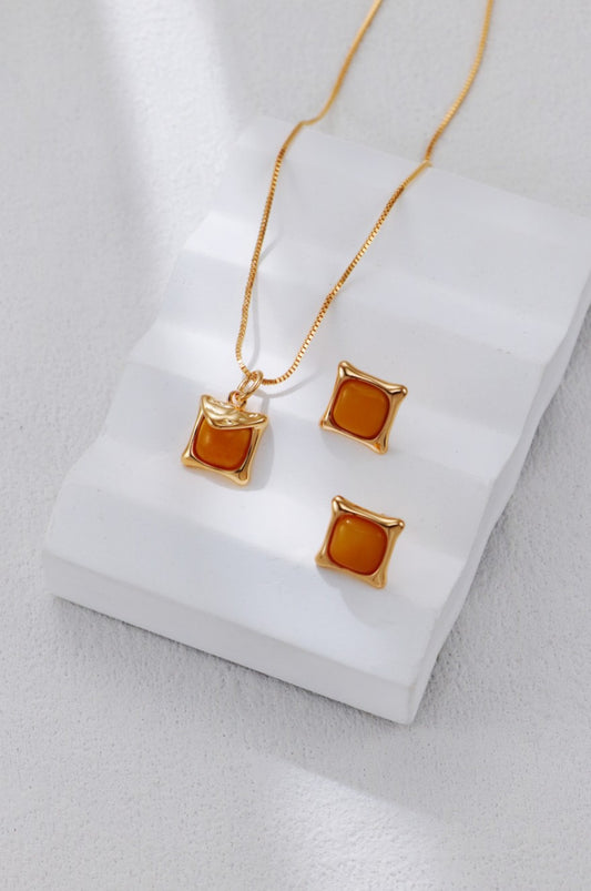 Gold necklace and earrings with amber-colored stones on a white surface