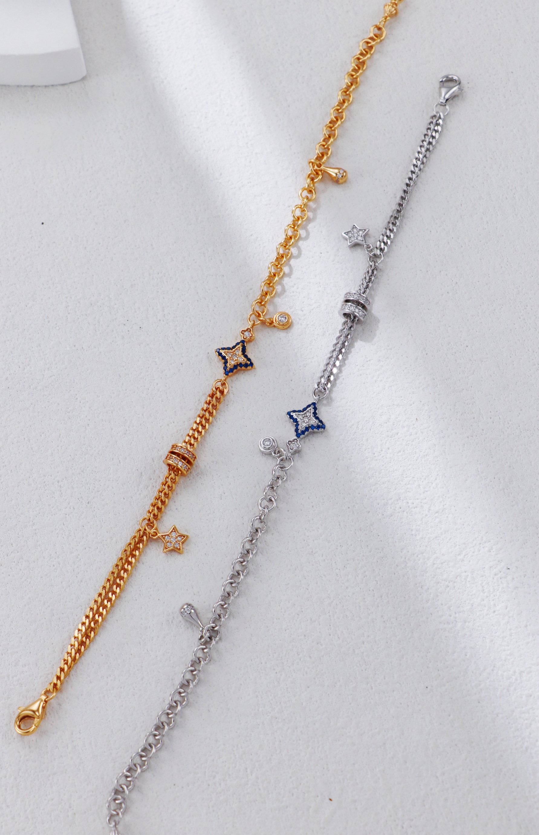 Two bracelets, one gold and one silver, with star-shaped charms on a light gray background.