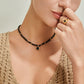 Woman wearing a black beaded necklace and ring against a neutral background
