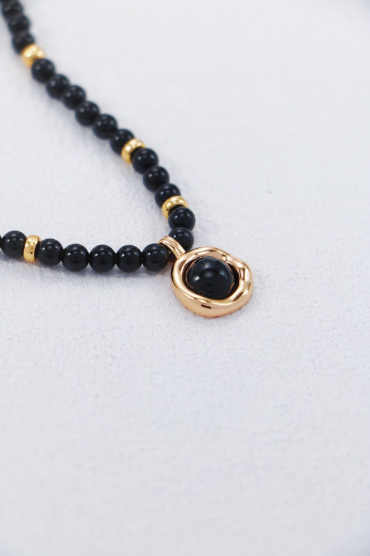 Black beaded necklace with a gold accent on a light gray background