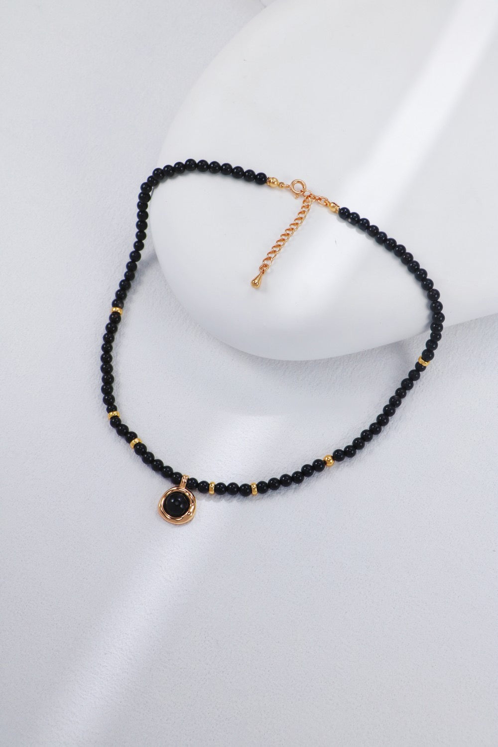 Black beaded necklace with gold accents on a white stand