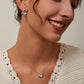 Woman wearing a heart-shaped necklace and earrings on a neutral background