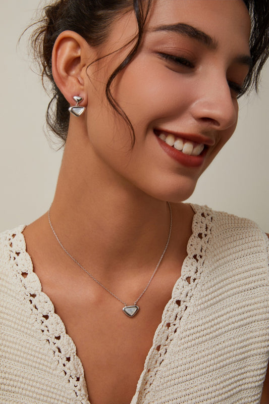 Woman wearing a heart-shaped necklace and earrings on a neutral background