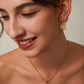 Woman wearing gold earrings and necklace on a neutral background