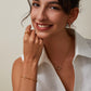 Woman wearing gold jewelry including a necklace, bracelet, and ring against a neutral background