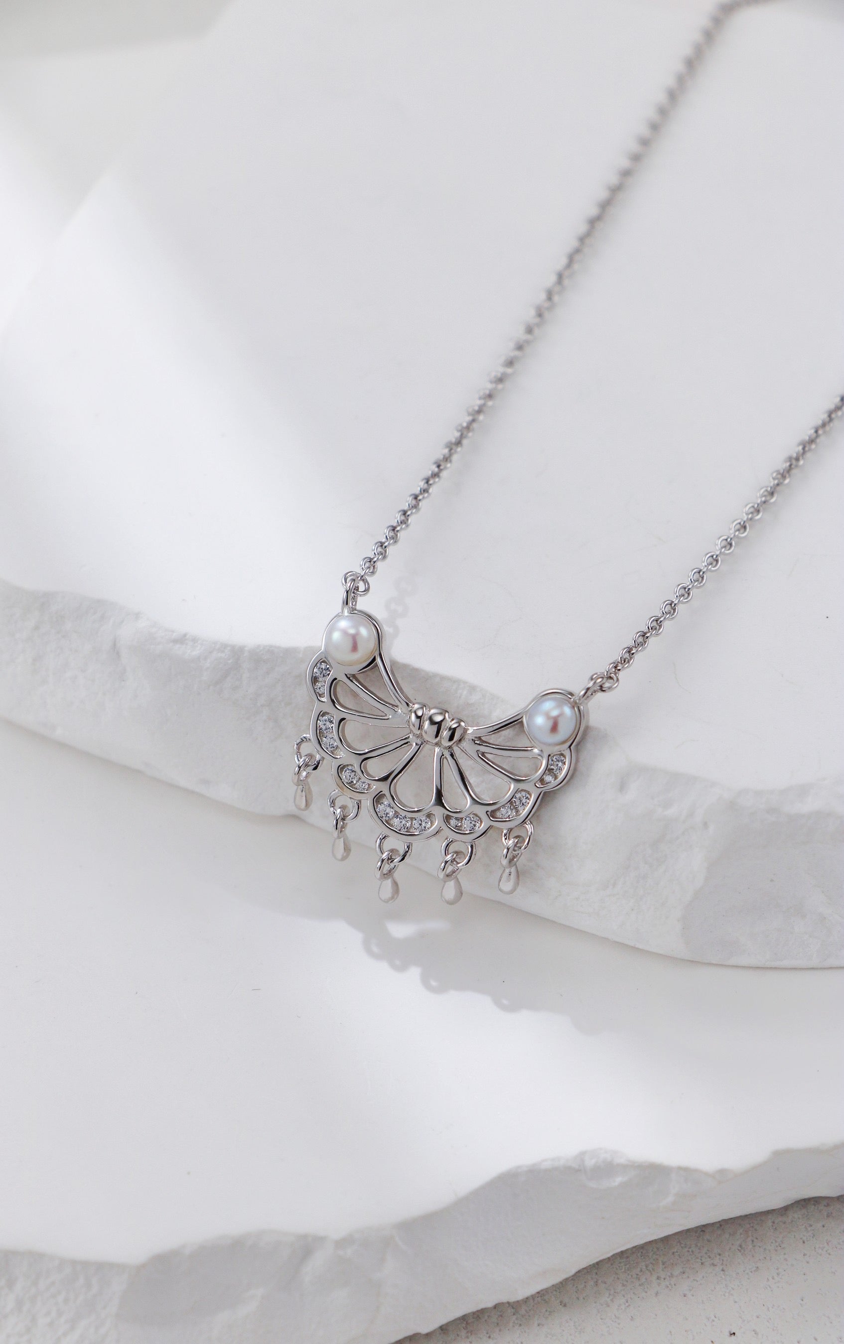 Silver necklace with butterfly design and pearls on a white background