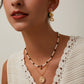 Close-up of a woman wearing gold earrings and necklaces against a neutral background