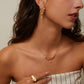 Woman wearing gold jewelry including earrings, necklace, and ring against a neutral background