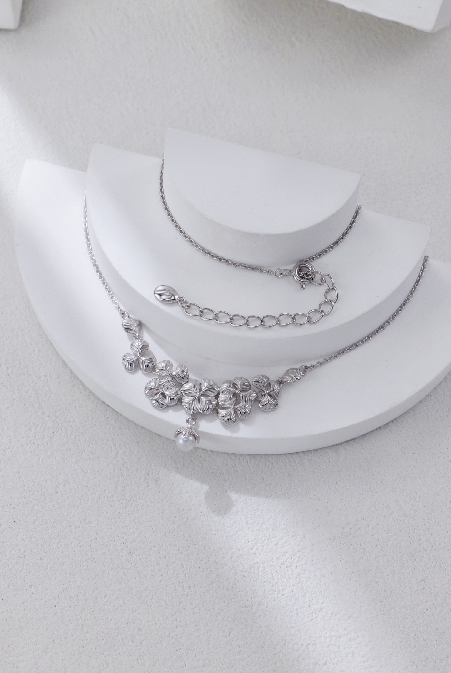 Silver necklace with floral design on a white stand