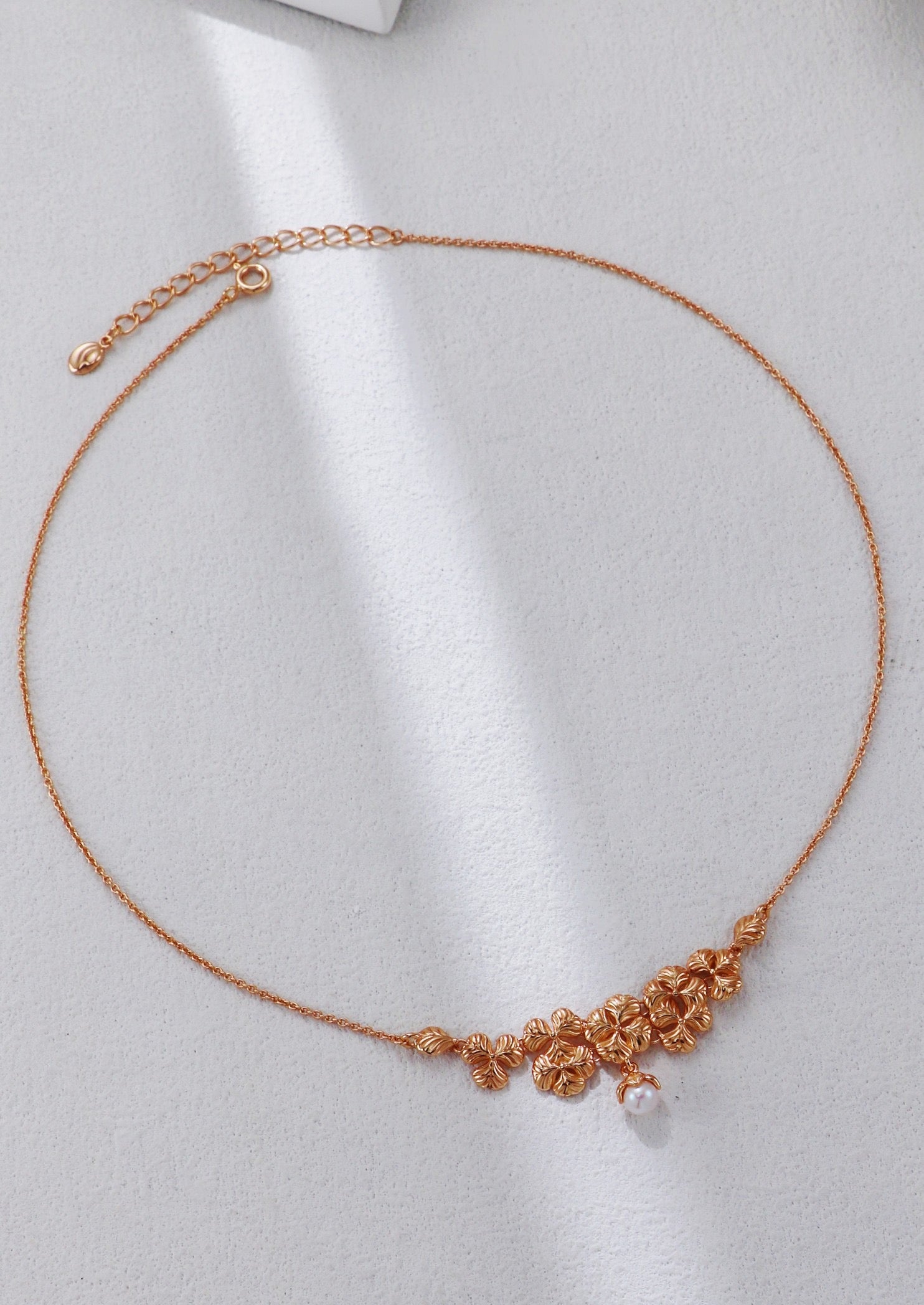 Rose gold necklace with floral design on a light gray background