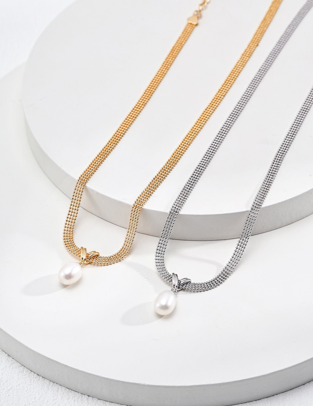 Two pearl necklaces on a white surface, one gold and one silver.