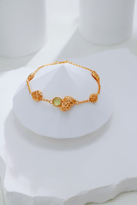 Gold bracelet with a green gemstone on a white mannequin bust.