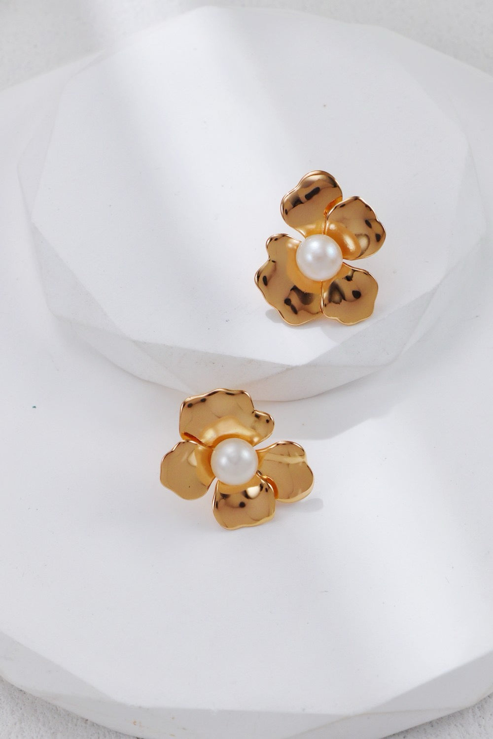 Gold flower-shaped earrings with pearl centers on a white background