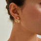 Close-up of a person wearing gold earrings with a neutral background