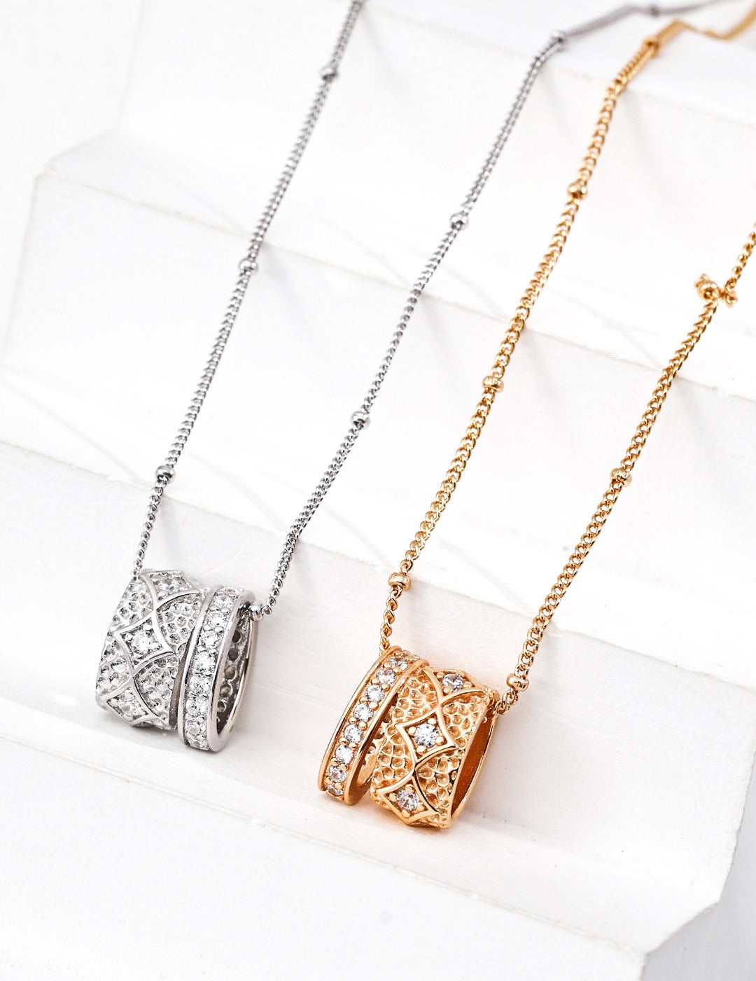 Two necklaces, one silver and one gold, on a white surface.